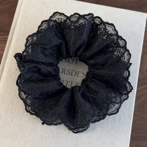 Close-up of black lace scrunchie with intricate floral embroidery on a white book