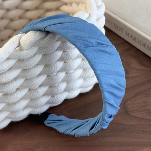 Detail of light blue pleated denim headband with soft fabric texture on a woven basket