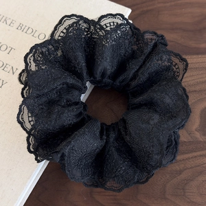 Detail of multi-layered black lace scrunchie with intricate floral embroidery on a wooden desk
