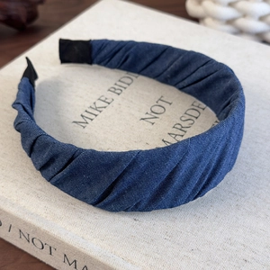 Detailed view of the dark blue denim pleated headband resting on a textured book