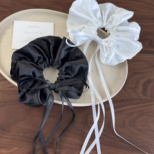 Detailed view of white and black satin scrunchies with long ribbons on a ceramic plate