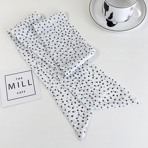Close-up of a white skinny scarf with black polka dots on a minimalist white desk