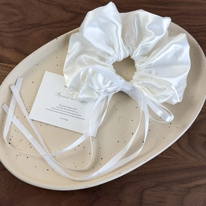 Detail of white satin scrunchie with long ribbons on a ceramic tray over dark wood