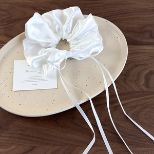 Detailed view of an ivory satin scrunchie with long ribbons on a ceramic plate
