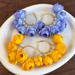 Detail view of large hoop earrings featuring floral petals and white pearls on a tray
