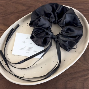 Close-up of a black satin scrunchie with long ribbons on a ceramic tray over wood