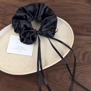 Close-up of black satin scrunchie with long ribbon bow on a beige ceramic tray