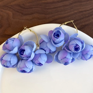 Detail of blue fabric rosebud wreath earrings with gold hoops on white ceramic
