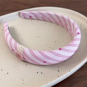 Gros plan d'un serre-tête en tissu rayé rose avec bordure en dentelle et bouton
