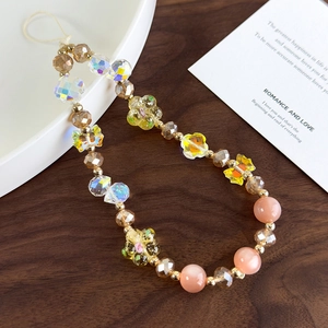 Detail of beaded phone wristlet with aurora crystal flowers and bow charms on wooden desk