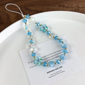 Detail view of handmade blue floral glass beaded phone strap on wooden background