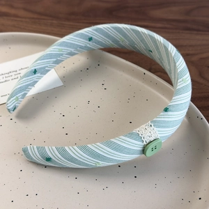 Détail d'un serre-tête en tissu rayé vert et blanc avec bordure en dentelle et bouton