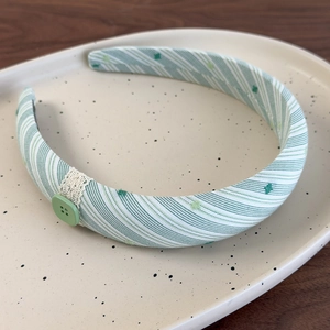 Détail d'un serre-tête en tissu rayé vert avec dentelle et bouton sur plat céramique