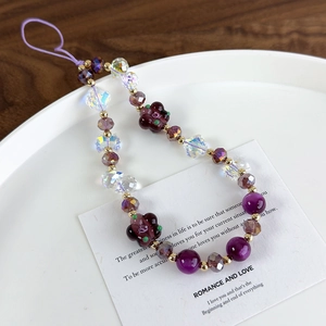 Detail of purple handmade beaded phone strap with floral charms on a white ceramic plate