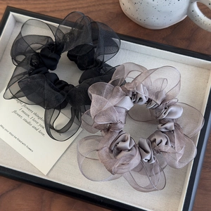 Detail of two layered organza scrunchies in black and pink on a wooden surface