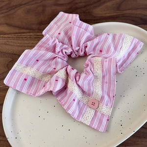 Détail du chouchou rayé rose avec bordure en dentelle et bouton sur plateau céramique