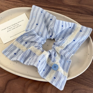 Détail d'un chouchou à rayures bleues avec bordure en dentelle et bouton décoratif