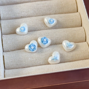 Detailaufnahme herzförmiger Perlenohrringe mit blauen Harzblumen und Seesternen