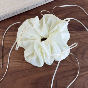 Détail d'un chouchou en organza crème avec de longs rubans sur une surface en bois
