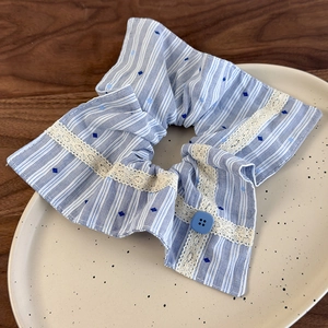 Détail d'un chouchou en tissu rayé bleu avec bordure en dentelle et bouton décoratif