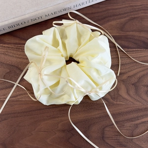 Détail d'un chouchou en organza jaune crème avec de délicats rubans sur bois sombre