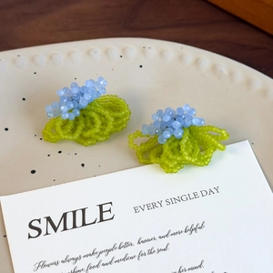 Close-up of handmade blue crystal and green bead flower stud earrings on a ceramic dish