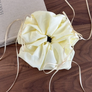 Détail d'un chouchou en organza jaune clair avec un nœud en ruban sur une table en bois