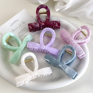 Close-up of six colorful acetate bow hair claws with marble texture in a white dish