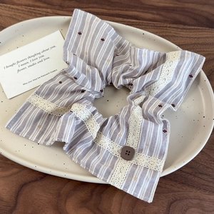 Détail d'un chouchou rayé avec bordure en dentelle et bouton marron sur une assiette