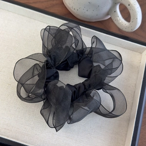 Macro shot of fluffy black organza scrunchie with layered pleated texture on white tray
