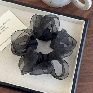 Macro detail of high-quality black organza scrunchie with pleated texture on elegant tray