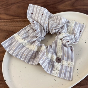 Détail d'un chouchou en tissu à rayures marron avec bordure en dentelle et bouton décoratif