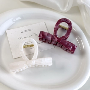 Detail of elegant bow hair claws in cream white and burgundy with marble texture