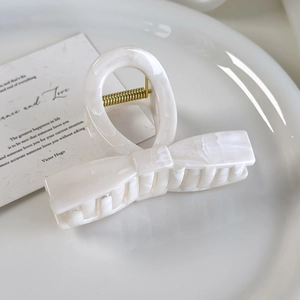 Close-up of cream marble effect bow hair claw clip with golden spring on ceramic tray