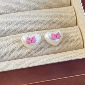 Nahaufnahme von Herz-Perlenohrringen mit rosa Schleifen auf einer beigen Schmuckschatulle
