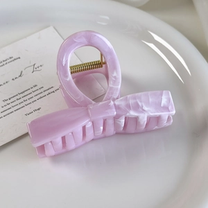 Close-up of pink marble acetate bow hair claw clip with golden metal spring details