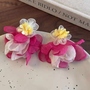 Detail of layered pink mesh flower earrings with yellow stamen on white ceramic plate