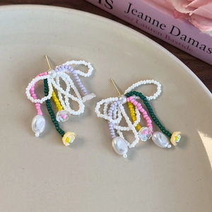 Détail de boucles d'oreilles nœuds en perles avec pompons colorés et pendentifs