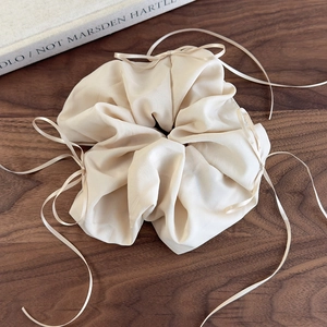 Détail du chouchou en organza champagne avec nœud et ruban sur fond en bois naturel