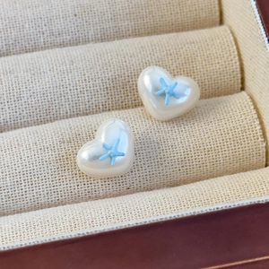 Nahaufnahme der herzförmigen Perlenohrringe mit kleinen blauen Seestern-Details auf Box