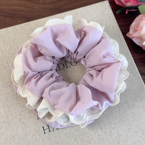 Dettaglio scrunchie lilla con pizzo bianco a onde su sfondo in tessuto beige testurizzato
