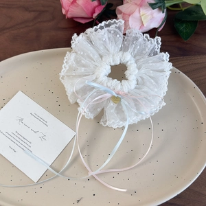 Dettaglio dello scrunchie in pizzo bianco con nastri pastello e ciondolo a cuore