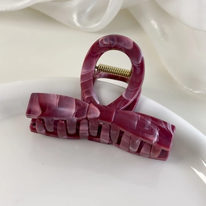 Detail of dark burgundy marble textured acetate hair claw clip on white silk