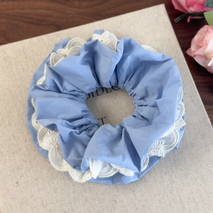 Dettaglio dello scrunchie in pizzo celeste con ricamo bianco e volant eleganti