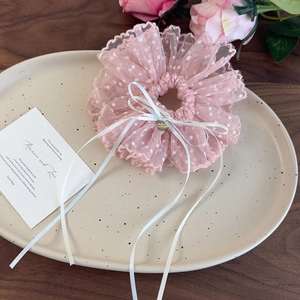 Dettaglio di elastico in pizzo rosa a pois con ciondolo a cuore dorato e fiocco