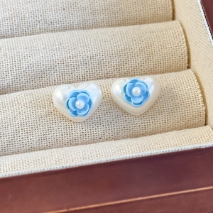 Makroaufnahme von herzförmigen Perlenohrringen mit blauer Rose und filigranen Details
