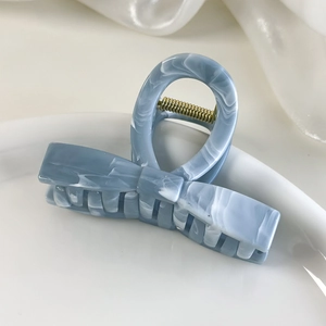 Close-up of grey-blue marble texture bow hair claw clip with golden metal spring