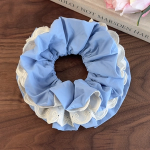 Dettaglio di un elastico azzurro a pieghe con ricamo in pizzo bianco su sfondo legno