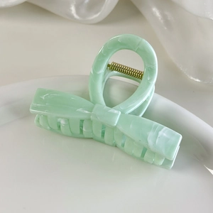 Detail of light green marble-textured bow hair claw clip on a white decorative dish
