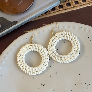 Macro shot of handmade beige woven straw hoop earrings on a ceramic jewelry tray